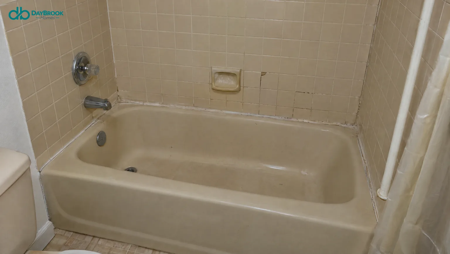 Dated almond bathtub with a beige tile surround and cracked grout, typical of a 1990s Maryland bathroom